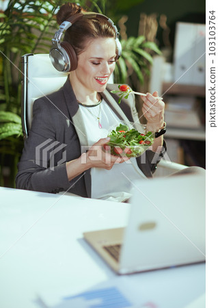 smiling female employee in green office eating salad 103103764