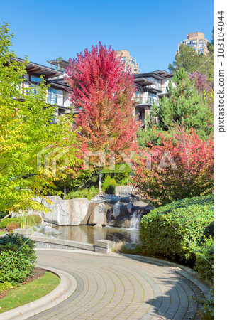 Paved pathway in residential area beside small waterfall on autumn day Paved pathway in residential area beside small waterfall on autumn day 103104044