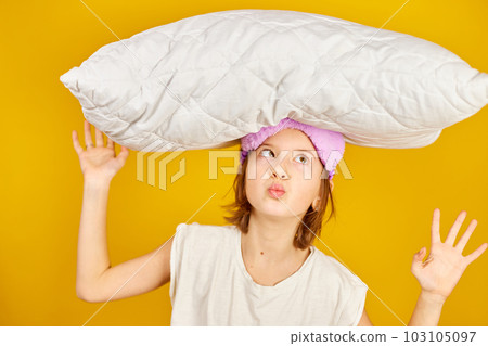 Funny teenage girl in white pyjamas with a violet sleeping mask hold pillow 103105097