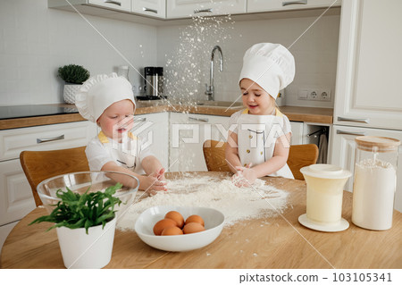 Adorable boy ad girl in chefs hats and aprons playing with the flour in the kitchen 103105341