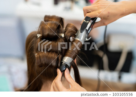 The hairdresser curls the model's hair. Curling iron for curling hair close-up. The hairdresser curls the model's hair. Curling iron for curling hair close-up. 103105556
