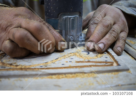 Close Up of Man Hands carving on wooden furniture. Carpenter using tool making Artistic Wood Carving. Producing an Ornament on Wood with Chisel and Hammer on a Panel of Wood . High quality photo 103107108