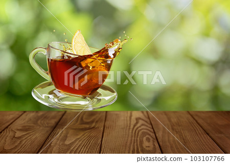 glass cup of tea with splash and slice of lemon on wooden table glass cup of tea with splash and slice of lemon on wooden table 103107766