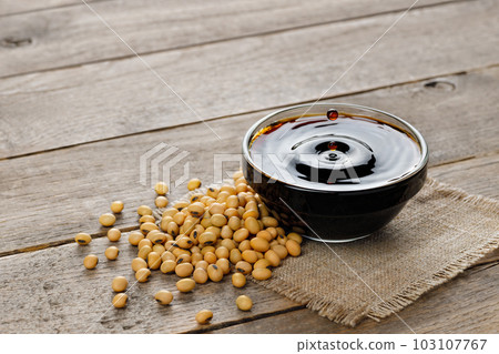 soy sauce in glass bowl with falling drops and dry soybeans on table soy sauce in glass bowl with falling drops and dry soybeans on table 103107767
