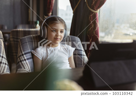 Happy baby girl 5 years old in headphones with tablet is sitting in cafe Happy baby girl 5 years old in headphones with tablet is sitting in cafe 103110342