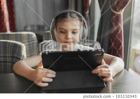 Girl 5 years old in headphones with tablet is sitting in cafe Girl 5 years old in headphones with tablet is sitting in cafe 103110343