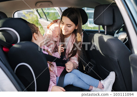 Attractive young mother put her daughter in a car seat and fastens her seat belts. Woman care about kid. Protection during the trip in the car. Attractive young mother put her daughter in a car seat and fastens her seat belts. Woman care about kid. Protection during the trip in the car. 103111094