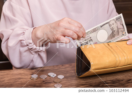 [一位家庭主婦從她的長錢包裡拿出一張 10,000 日元的鈔票，裡面有硬幣] 103112494