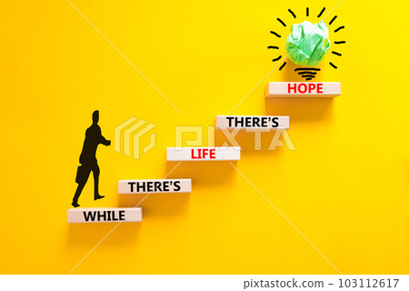Life and hope symbol. Concept word While there is life there is hope on wooden block. Beautiful yellow table yellow background. Businessman icon. Business lifestyle life and hope concept. Copy space. Life and hope symbol. Concept word While there is life there is hope on wooden block. Beautiful yellow table yellow background. Businessman icon. Business lifestyle life and hope concept. Copy space. 103112617