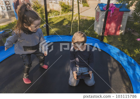 children sit on a trampoline and look at the phone 103115786