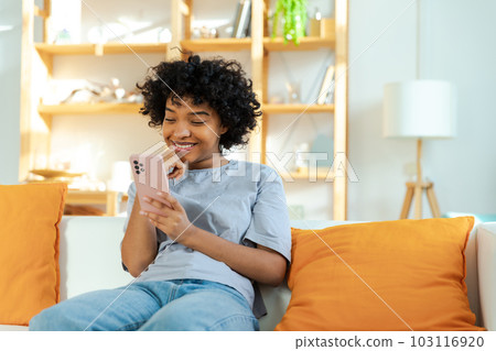 African girl holding smartphone touch screen typing scroll page at home. Woman with cell phone surfing internet using social media apps playing game. Shopping online Internet news cellphone addiction 103116920