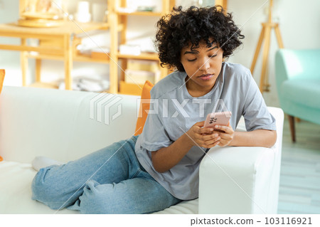 African girl holding smartphone touch screen typing scroll page at home. Woman with cell phone surfing internet using social media apps playing game. Shopping online Internet news cellphone addiction African girl holding smartphone touch screen typing scroll page at home. Woman with cell phone surfing internet using social media apps playing game. Shopping online Internet news cellphone addiction 103116921