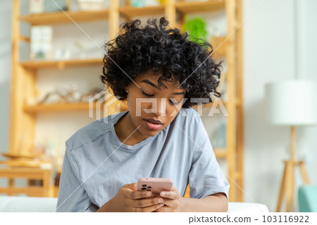 African girl holding smartphone touch screen typing scroll page at home. Woman with cell phone surfing internet using social media apps playing game. Shopping online Internet news cellphone addiction African girl holding smartphone touch screen typing scroll page at home. Woman with cell phone surfing internet using social media apps playing game. Shopping online Internet news cellphone addiction 103116922