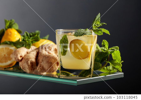 Ginger ale beer cocktail with lemon and mint in a frozen glass on a black background. Ginger ale beer cocktail with lemon and mint in a frozen glass on a black background. 103118045