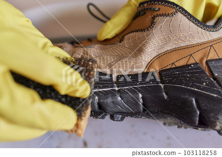 A person is cleaning men's suede casual boots with brush, sponge and spray. Shoe shine and care. Footwear moisture and dirt protection. A person is cleaning men's suede casual boots with brush, sponge and spray. Shoe shine and care. Footwear moisture and dirt protection. 103118258