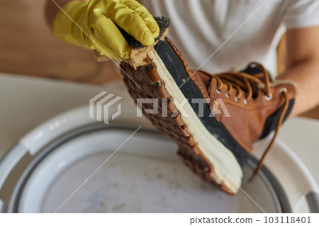 A person is cleaning men's suede casual boots with brush, sponge and spray. Shoe shine and care. Footwear moisture and dirt protection. A person is cleaning men's suede casual boots with brush, sponge and spray. Shoe shine and care. Footwear moisture and dirt protection. 103118401