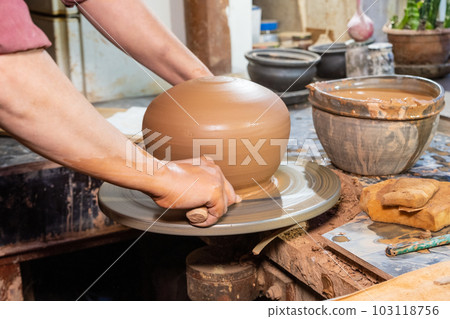 ceramics, workshop, ceramic art concept - close-up of man's hands forming a new vessel, man's fingers working with potter's wheel and raw edge, frontal close-up. 103118756
