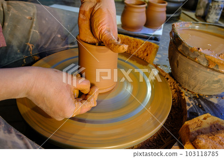 ceramics, workshop, ceramic art concept - close-up of man's hands forming a new vessel, man's fingers working with potter's wheel and raw edge, frontal close-up. 103118785