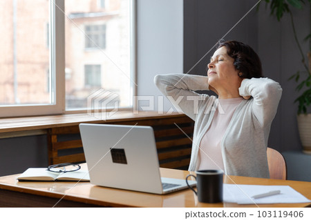 Middle aged senior woman at home relaxing stretching hands and body taking break from work on laptop. Older mature woman happy after work done satisfied by good result. Fatigue from long laptop usage Middle aged senior woman at home relaxing stretching hands and body taking break from work on laptop. Older mature woman happy after work done satisfied by good result. Fatigue from long laptop usage 103119406