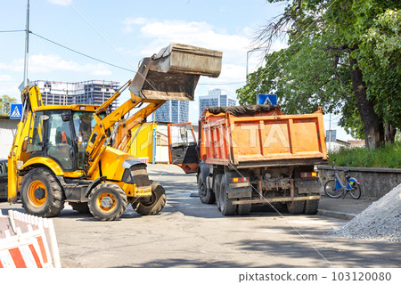 Construction road machinery, a tractor with a hydraulic bucket and an old truck at a fork in a city street on a sunny day. 103120080