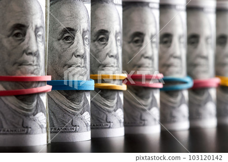 A row of rolled hundred dollar bills with rubber bands on dark background A row of rolled hundred dollar bills with rubber bands on dark background 103120142