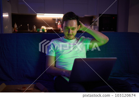 Handsome young man eating unhealthy food while watching movie at night. 103120674