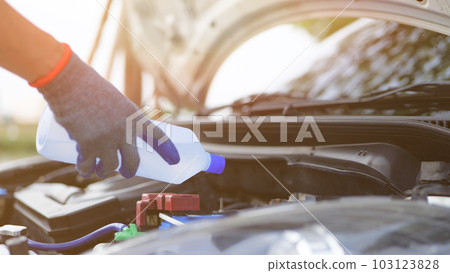 Man holding distilled or deionized water to refill car battery. Car inspection and maintenance concept. Man holding distilled or deionized water to refill car battery. Car inspection and maintenance concept. 103123828