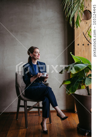 Portrait of young woman sitting near window in green office full of plants. 103124445
