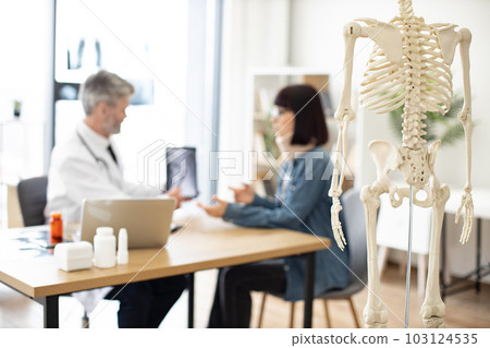 Skeleton in exam room of hospital with people in background Skeleton in exam room of hospital with people in background 103124535