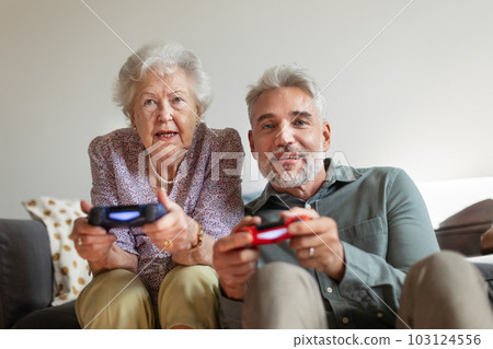 Mature man playing video games with his senior mother, having fun. Mature man playing video games with his senior mother, having fun. 103124556