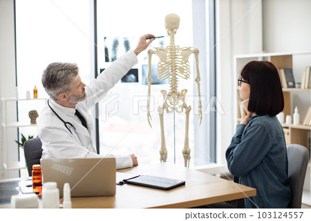 Doctor showing injury site to patient using skeleton Doctor showing injury site to patient using skeleton 103124557