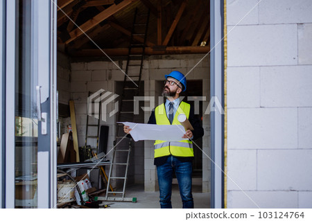 Mature businessman controlling blueprints from unfinished house. 103124764