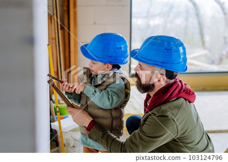 Father and his little son working on their unfinished house. 103124796