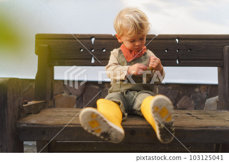 Little boy in overalls sitting on bench and eating homegrown grapes. Little boy in overalls sitting on bench and eating homegrown grapes. 103125041