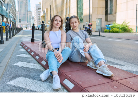 Two smiling female students looking at camera, modern urban style, road, buildings background Two smiling female students looking at camera, modern urban style, road, buildings background 103126189