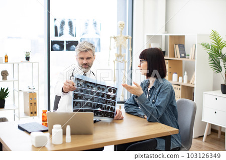 Doctor examining MRI scans while woman sitting at desk 103126349