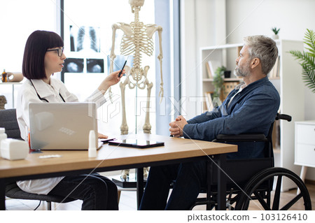 Female doctor talking to male in wheelchair using skeleton Female doctor talking to male in wheelchair using skeleton 103126410