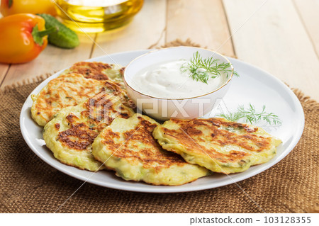 Vegan zucchini pancakes in plate and cream sauce on wooden background. Healthy vegan diet food. Vegan zucchini pancakes in plate and cream sauce on wooden background. Healthy vegan diet food. 103128355