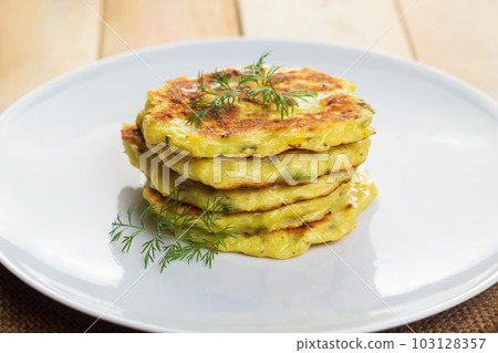 Stack of zucchini pancakes on white plate. Green vegetarian fritters. 103128357
