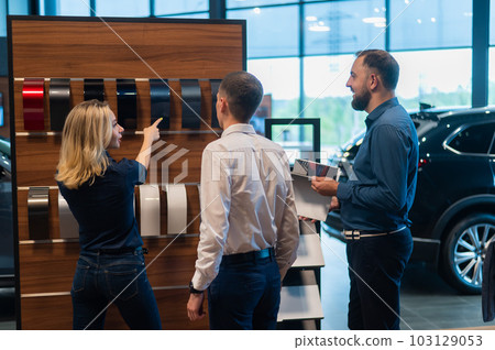 The seller helps a married couple choose the color of a new car.  103129053