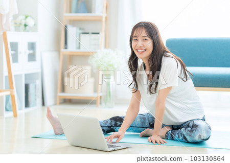 Young woman doing online yoga while looking at computer in living room 103130864