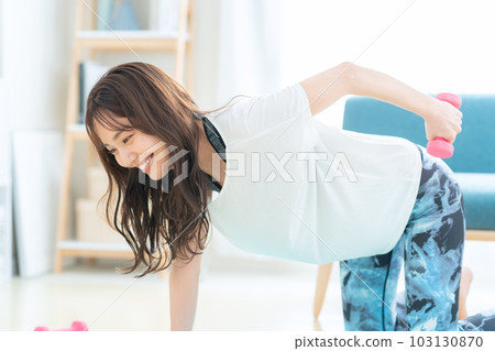 在客廳裡用啞鈴進行肌肉訓練的年輕女性 103130870