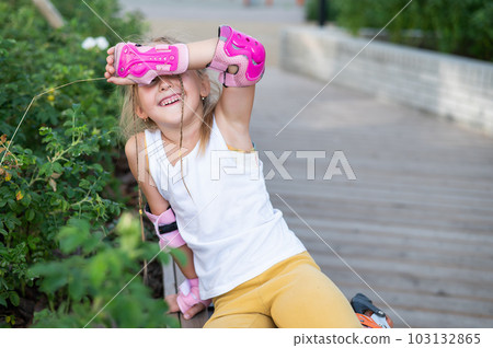 A little Caucasian girl in roller skates sits on a bench. A little Caucasian girl in roller skates sits on a bench. 103132865