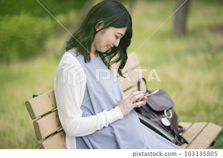 Pregnant woman looking at smartphone in the park Pregnant woman looking at smartphone in the park 103135805