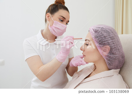 Cosmetologist drawing mark on client face to prepare for rejuvenation treatment 103138069