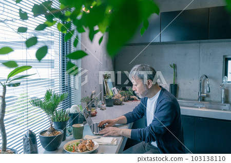 Middle-aged man working on a computer in the kitchen in the morning Middle-aged man working on a computer in the kitchen in the morning 103138110