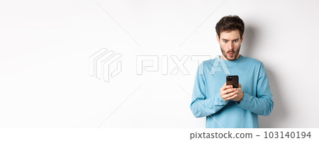 Amazed young man staring at smartphone screen and saying wow, looking at online offer, standing on white background 103140194