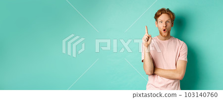 Pensive redhead man in t-shirt raising index finger, gasping as pitching at idea, saying suggestion, standing over turquoise background Pensive redhead man in t-shirt raising index finger, gasping as pitching at idea, saying suggestion, standing over turquoise background 103140760