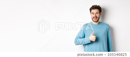 Cheerful young man agree and say yes, show thumb up in approval, smiling happy at camera, standing over white background 103140825