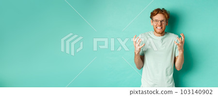 Portrait of distressed and angry redhead guy losing temper, shouting and shaking hands outraged, staring with furious face at camera, standing over mint background 103140902
